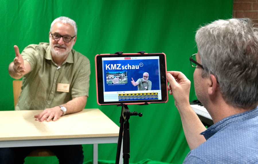 Dies ist ein Bild zeigt 2 Personen beim drehen einer Nachrichtensendung mit dem iPad vor einem Greenscreen Vorhang